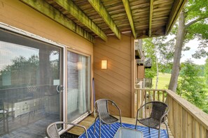 A covered outdoor area with a sliding glass door, two wicker chairs, a blue patterned rug, and a wooden deck railing. - Near Slopes, Golf, Lake! Shanty Creek Resort Condo (Bellaire)