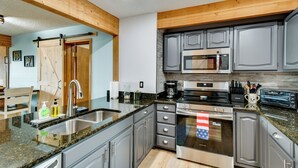 A modern kitchen with granite countertops, stainless steel appliances, and wooden beams. - Near Slopes, Golf, Lake! Shanty Creek Resort Condo (Bellaire)