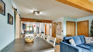 A dining area with a wooden table and chairs, a blue sofa, and a kitchen in the background. - Near Slopes, Golf, Lake! Shanty Creek Resort Condo (Bellaire)