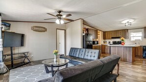 A modern living room with a black leather sofa, a glass coffee table, and a ceiling fan. - 9 Mi to Stockyards! Family Home in Fort Worth (Fort Worth)