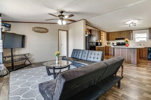 A modern living room with a black leather sofa, a glass coffee table, and a ceiling fan. - 9 Mi to Stockyards! Family Home in Fort Worth (Fort Worth)