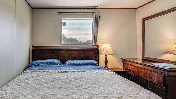 A hotel room with a bed, a nightstand, a lamp, a dresser, and a window with curtains. - 9 Mi to Stockyards! Family Home in Fort Worth (Fort Worth)