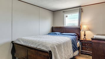 Een slaapkamer met een bed, nachtkastje, lamp en raam met gordijnen.