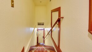 A hallway with a wooden staircase, a red carpet, and a door at the end. - Jasmine Arbor - 2BR Apt in Coveted Historic Dtwn (Savannah)