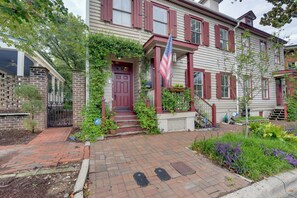 A two-story building with a red door, a flag, and a brick pathway leading to the entrance. - Jasmine Arbor - 2BR Apt in Coveted Historic Dtwn (Savannah)