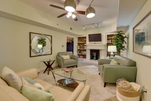 Un salon comprenant un canapé, des fauteuils, une table basse, une cheminée, un téléviseur et un ventilateur de plafond.