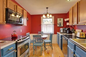 A kitchen with wooden cabinets, a microwave, an oven, a dining table with chairs, and a window with curtains. - Jasmine Arbor - 2BR Apt in Coveted Historic Dtwn (Savannah)