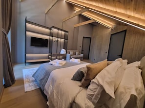 A modern bedroom with a large bed, a flat-screen TV, a seating area, and a wardrobe.