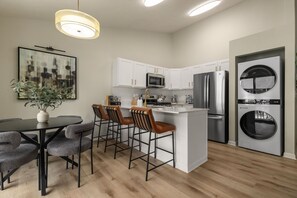 A modern kitchen with white cabinets, stainless steel appliances, and a central island with bar stools. - Luxury 2BR/2BA Condo |Walk to ND| Private Balcony (South Bend)