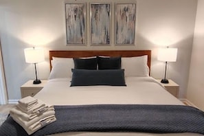 Ein ordentlich bezogenes Bett mit Holz-Kopfteil, zwei Nachttischlampen und einem Stapel gefalteter Handtücher am Rand.