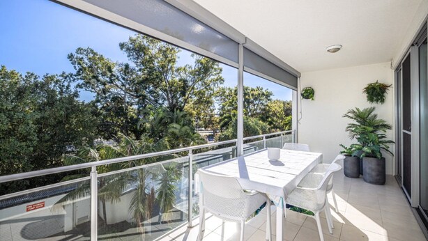 Ein Balkon mit Glasgeländer, einem Tisch, Stühlen und Topfpflanzen.