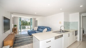 Eine moderne Wohnung mit Küche, einem Wohnbereich mit blauem Sofa und einem Balkon mit Blick.