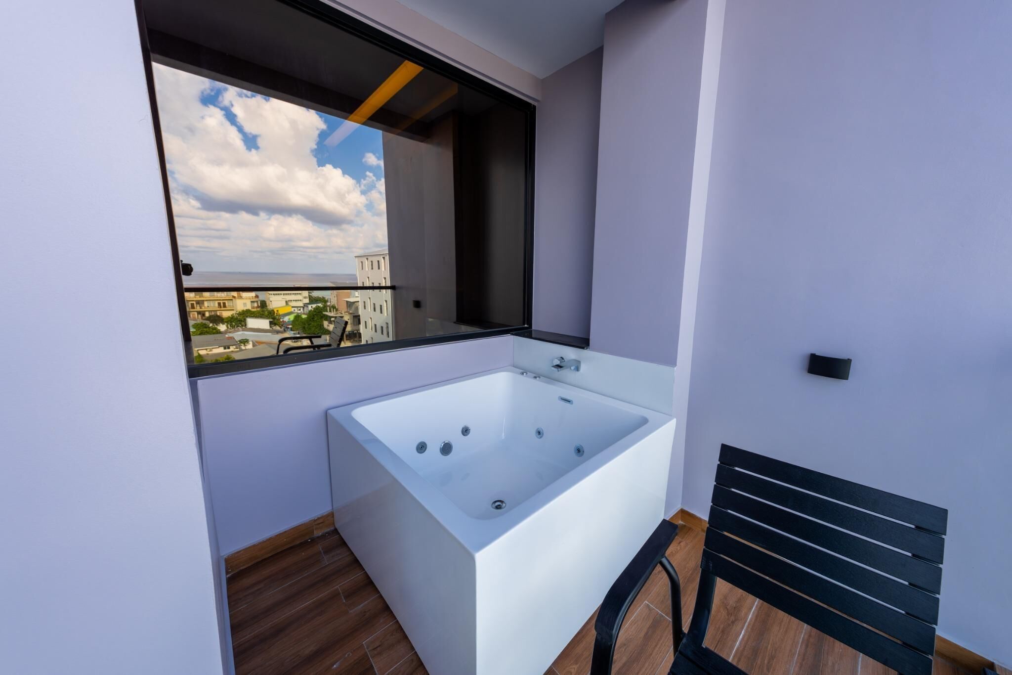 A modern bathroom with a bathtub, a window, and a view of buildings.
