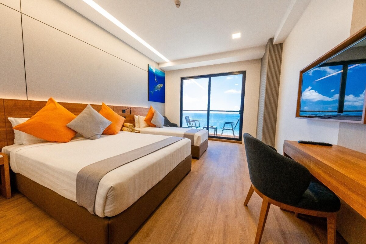 Habitació d'hotel amb dos llits, un escriptori, una cadira i un gran finestral amb vista al mar.