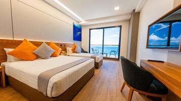 A hotel room with two beds, a desk, a chair, and a large window with a view of the sea.