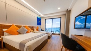 Una camera d'albergo con un letto grande, una scrivania, una sedia e vista sull'oceano attraverso un'ampia finestra.