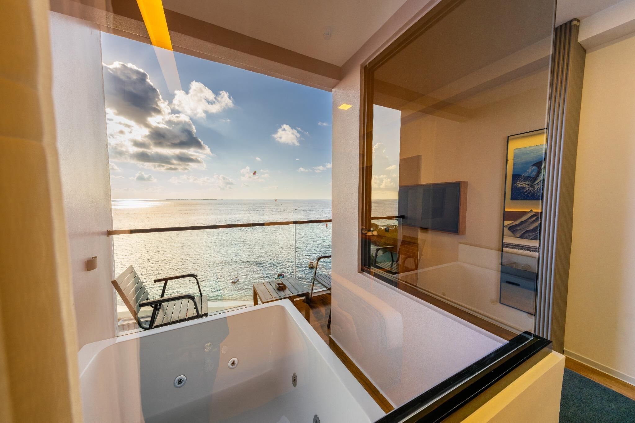 Un balcon avec vue sur la mer, une baignoire entourée de parois en verre et un téléviseur fixé au mur.