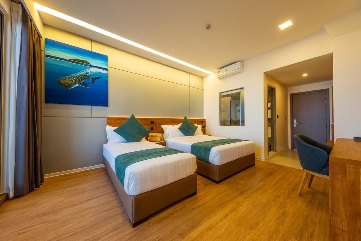 Habitació d'hotel amb dos llits, un escriptori i un quadre de peix a la paret.