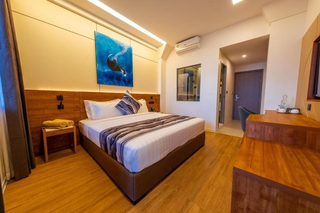 Una habitación de hotel moderna con una cama grande, suelo de madera, un cuadro en la pared y una mesita con una toalla.