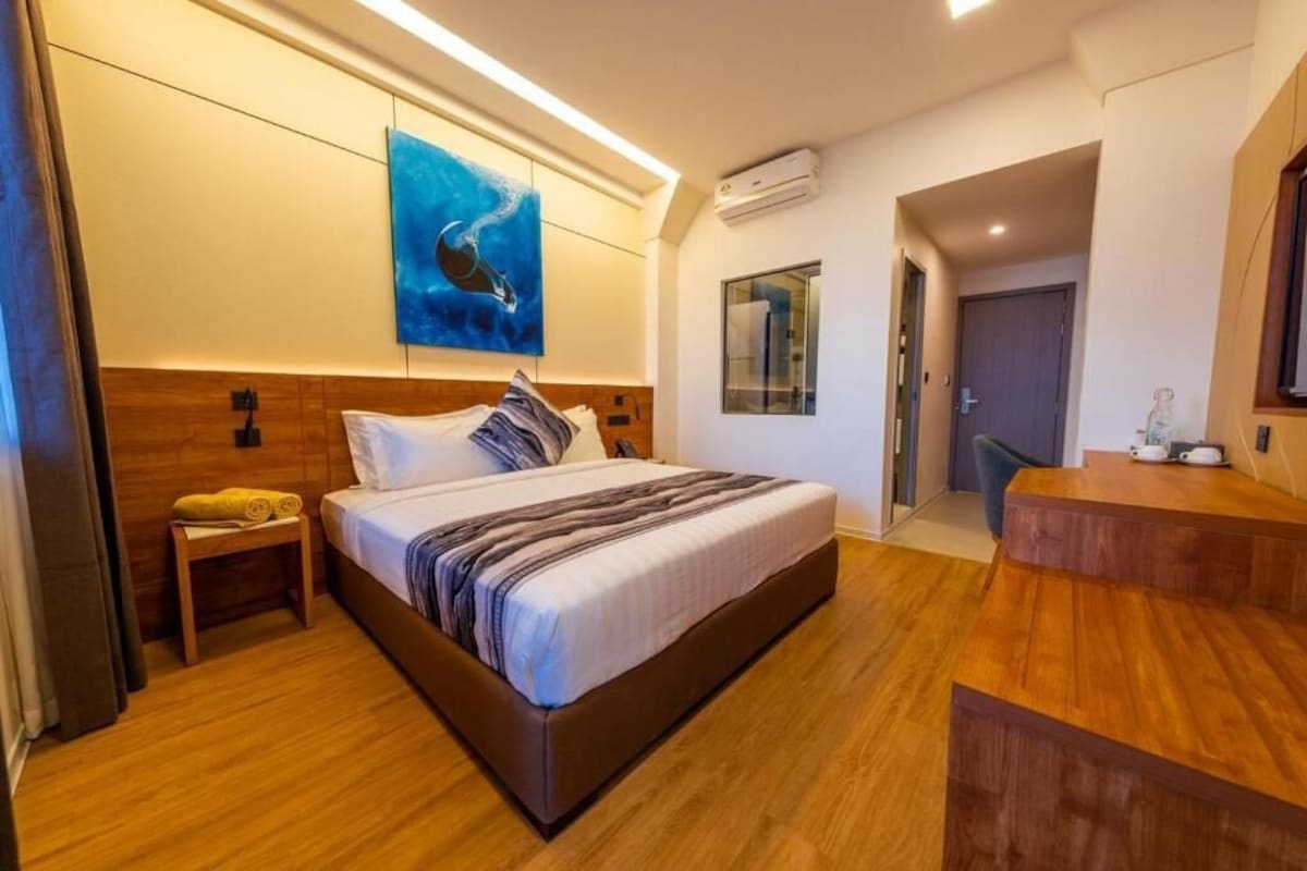 Una habitación de hotel moderna con una cama grande, suelo de madera, un cuadro en la pared y una mesita con una toalla.