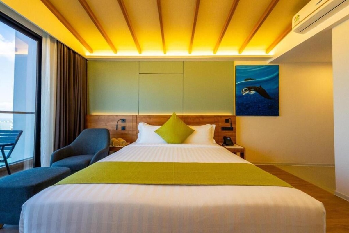 Habitació d'hotel amb un llit, una cadira, un quadre i una finestra.