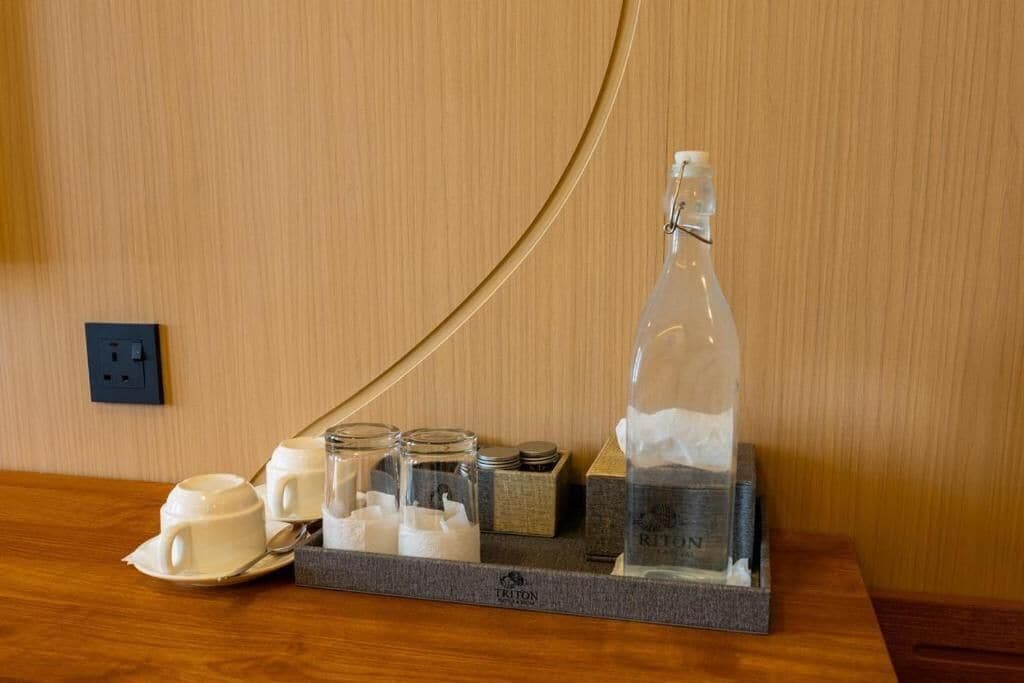 Preparación para el desayuno en una habitación de hotel, con una bandeja que contiene una botella, tazas y frascos.