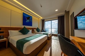 A hotel room with a bed, a desk, a chair, a TV, and a large window with a view of the sea. - Triton Exotica (Maafushi)