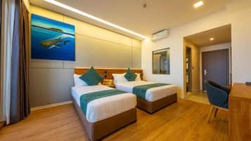 A hotel room with two beds, a desk, and a painting of a fish on the wall.