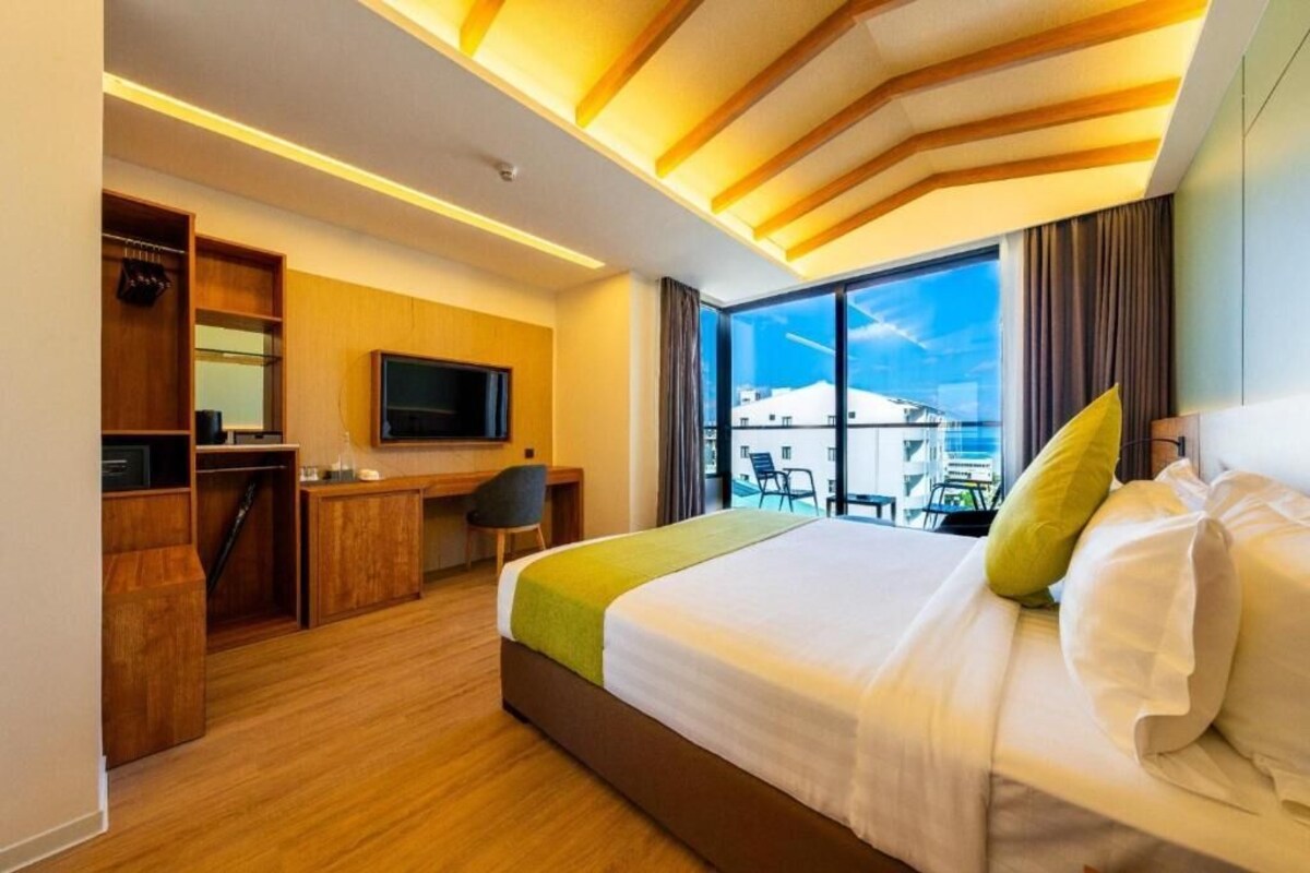 Habitación de hotel con cama, escritorio, televisor y vista a la ciudad.
