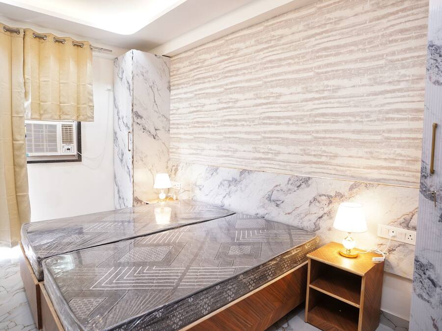 A bedroom with a bed, bedside tables, a wall-mounted air conditioner, and a window with curtains.