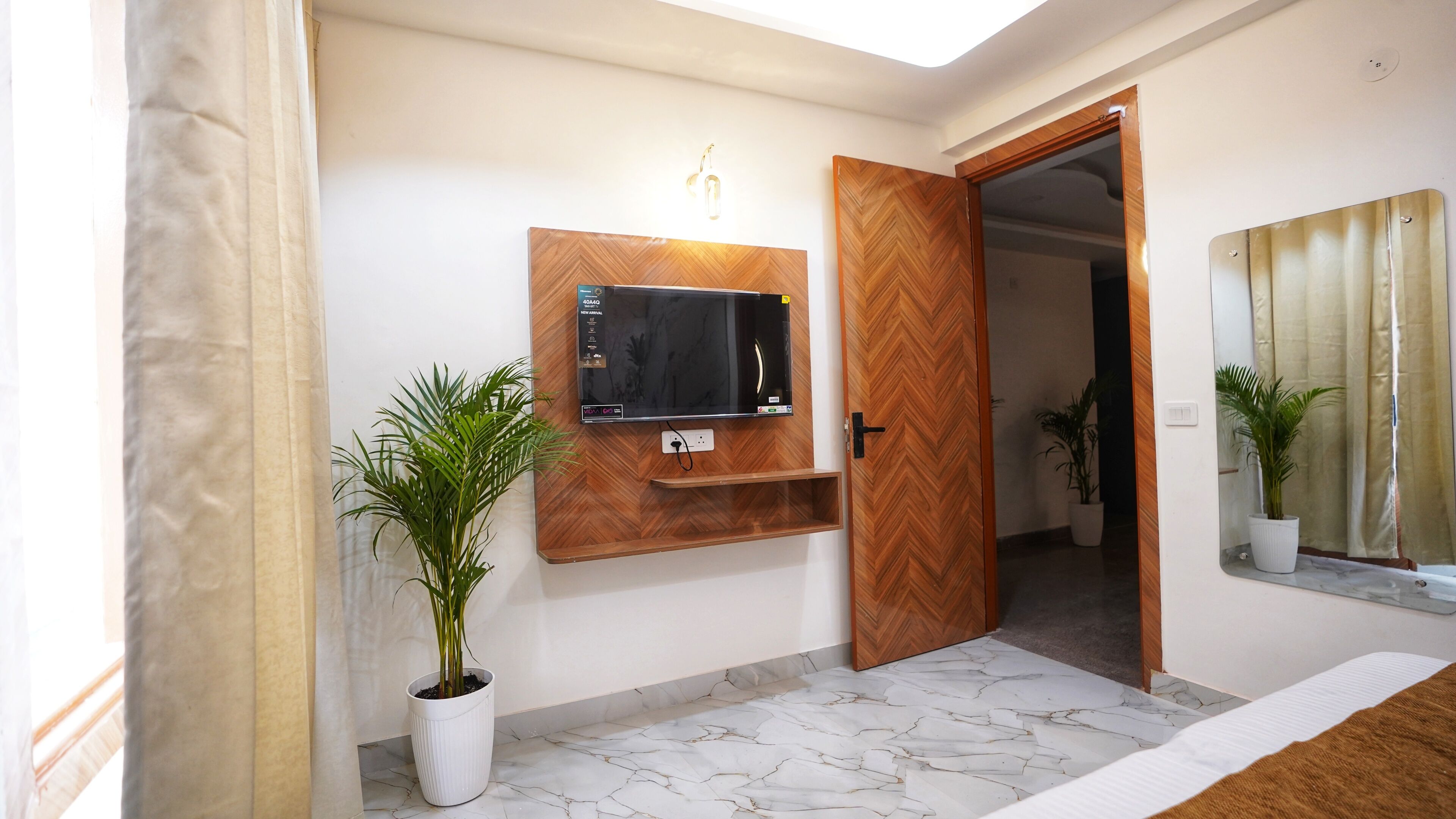 A room with a television mounted on a wooden panel, a potted plant, a mirror, and a marble floor.