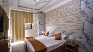 A hotel room with a bed, bedside table, lamp, air conditioning unit, and a ceiling fan.