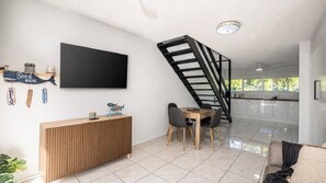 Ein modernes Wohnzimmer mit Flachbildfernseher, einer Holzkonsole, einem Essbereich mit Stühlen und einer Küche im Hintergrund.