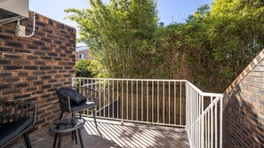 Een terras met een bakstenen muur, een wit metalen hek, een glazen tafel en een zwarte stoel.