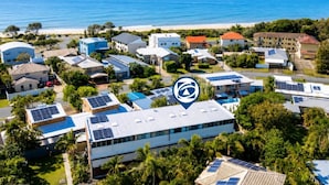 An aerial view of a residential area with multiple houses, some with solar panels, and a beach in the background. - Surf Sound Holiday Hideaway (WOORIM)