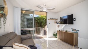 A living room with a sofa, a television mounted on the wall, and a ceiling fan.