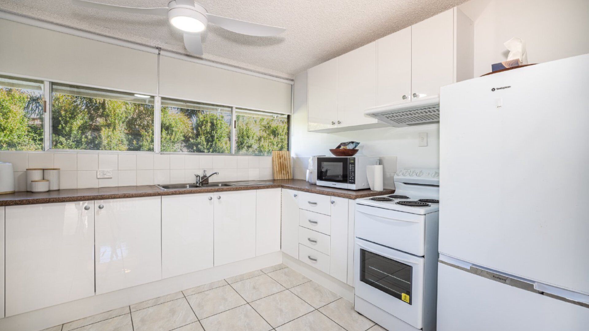 A modern kitchen with white cabinets, a microwave, stove, and a refrigerator.