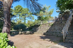 Escadaria de pedra que leva a um deck de madeira com guarda-corpo de metal, cercada por árvores e vegetação.