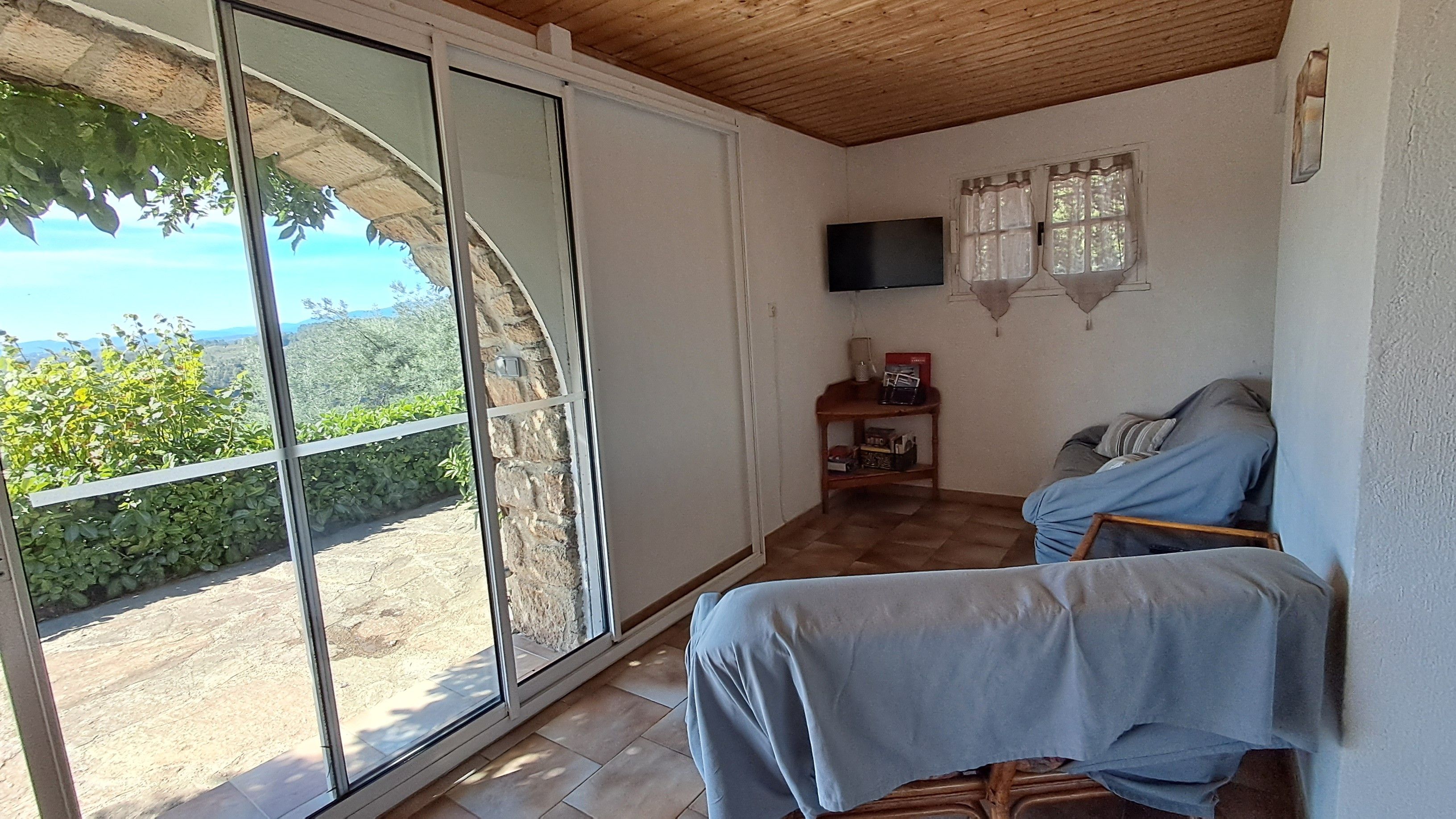 A room with a sliding glass door leading to a balcony, a television mounted on the wall, and a small wooden table with items on it.