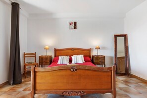 Ein Schlafzimmer mit einem hölzernen Bett, zwei Nachttischen, einem Sessel, einem Spiegel und einem Vorhang.