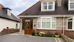 Une maison à deux étages avec une façade en pierre, une porte d’entrée dotée d’un panneau de verre et une allée pavée.