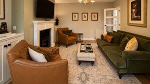 Un salon doté d’une cheminée, de fauteuils en cuir, d’un canapé vert et d’un téléviseur à écran plat fixé au-dessus de la cheminée.