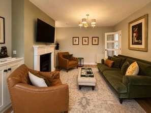A living room with a fireplace, leather armchairs, a green sofa, and a flat-screen TV mounted above the fireplace. - Apartment 91, Inverness (Inverness)