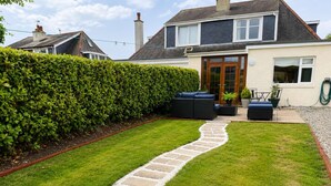 Un jardin bien entretenu, avec un chemin de pierre menant à un espace aménagé avec du mobilier d’extérieur.