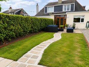 A well-maintained garden with a stone pathway leading to a seating area with outdoor furniture. - Apartment 91, Inverness (Inverness)