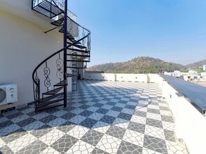 A rooftop terrace with a black spiral staircase, tiled flooring, and a view of a hill. - Palette Hotel Sun Royaale Udaipur (Udaipur)