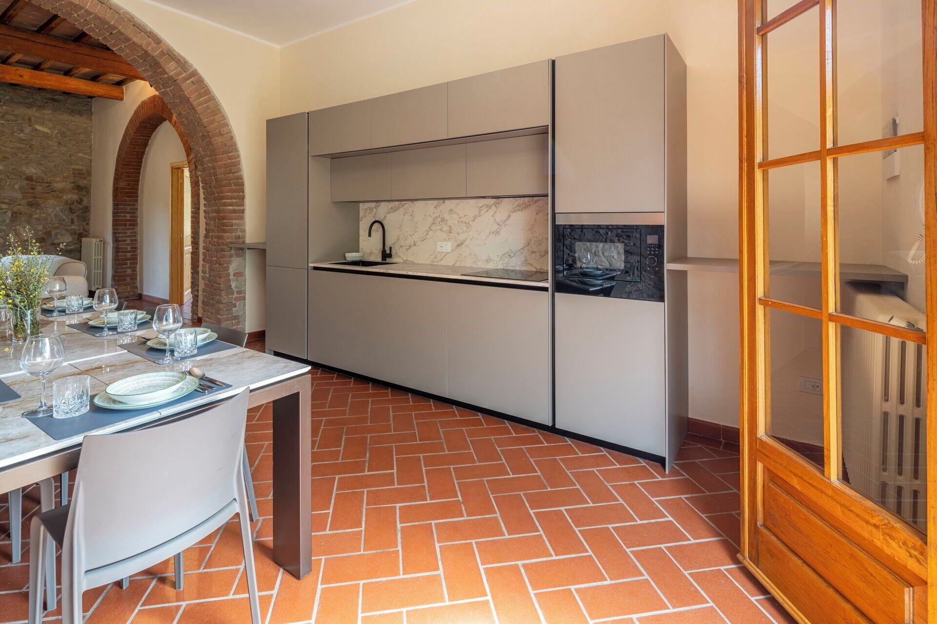 Une cuisine moderne avec des meubles gris, un pare-feu en marbre et un sol carrelé.