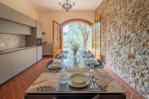 A modern kitchen with a dining area, stone walls, and a view of trees.
