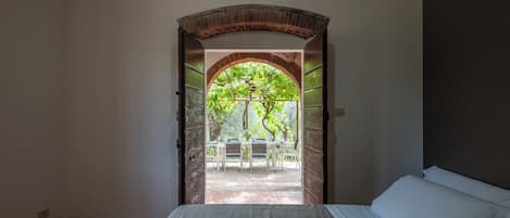 Una habitación con una cama y un arco de ladrillo que da a un espacio exterior con una mesa y sillas.