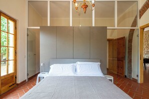 A bedroom with a large bed, a chandelier, and a view of a brick wall. - Casale delle Lupe by Geco Vacation Rentals (Campiglia Marittima)